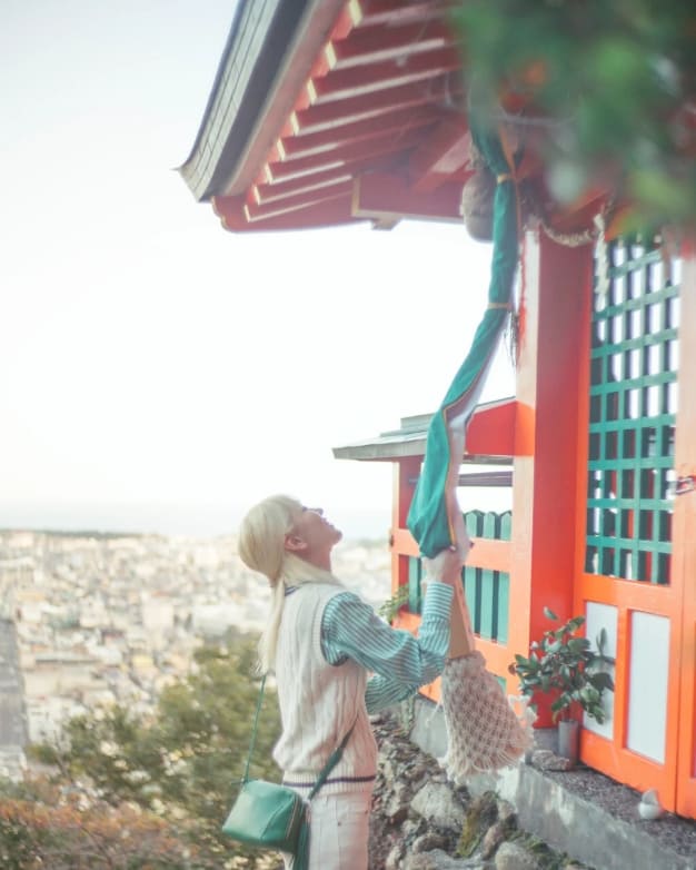 神社の鐘を鳴らす女性の写真